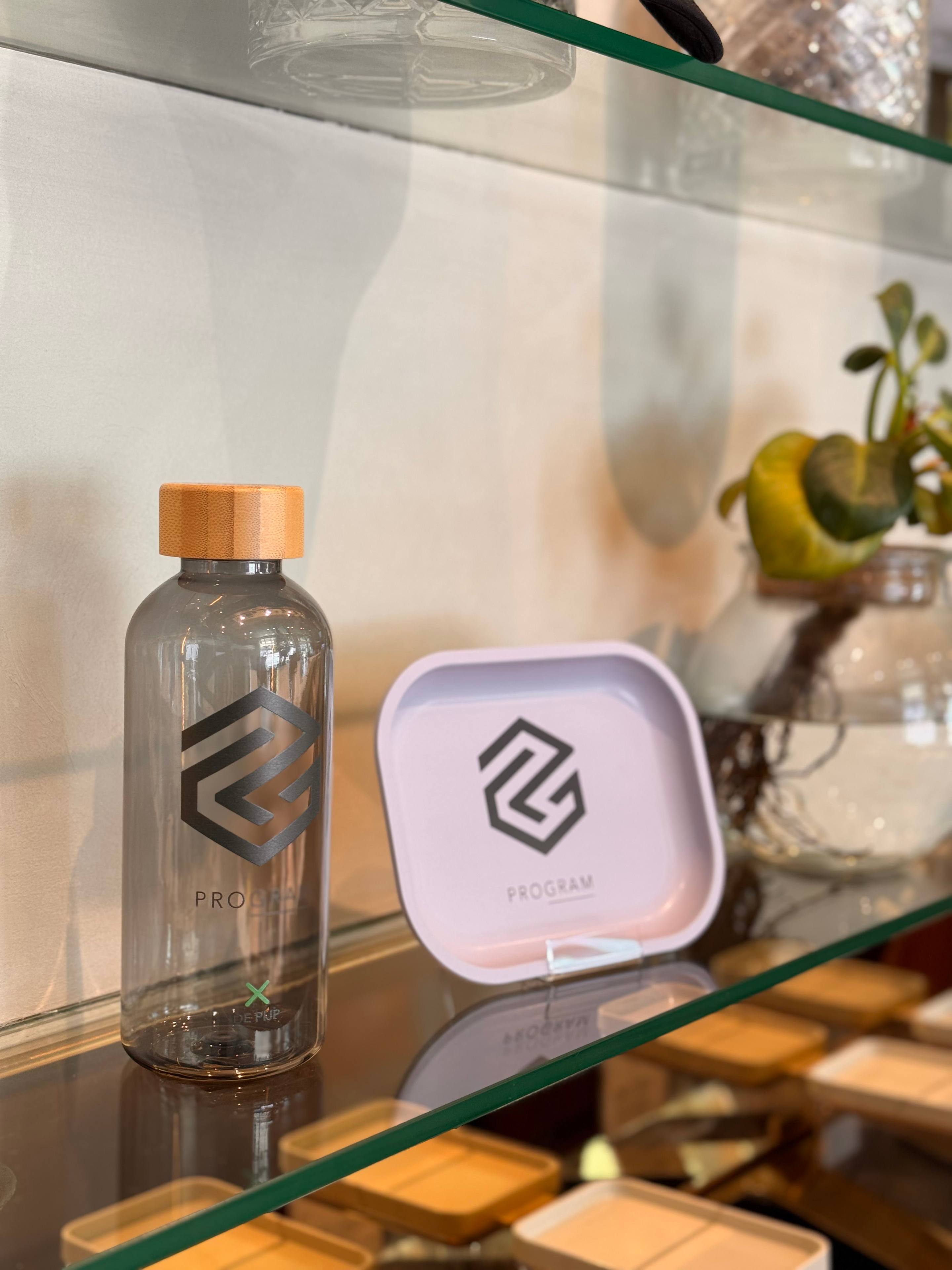 PROGRAM merch bottle and tray on a glass shelf